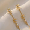 Gold star and bar drop earrings laid on fabric, AllureNL